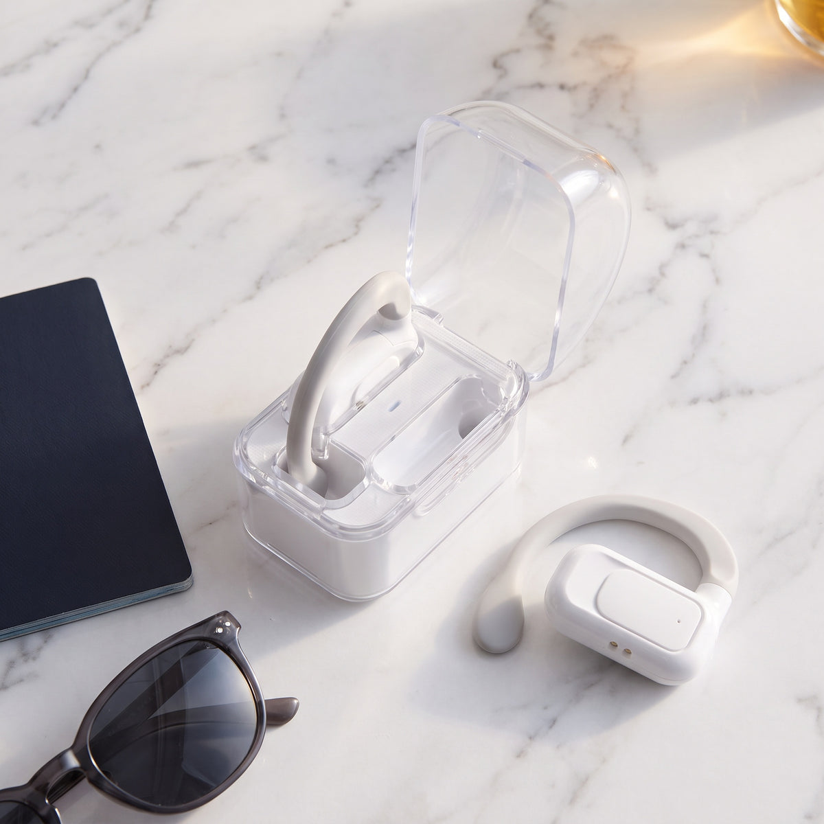Earbuds and open case on marble beside a passport and sunglasses